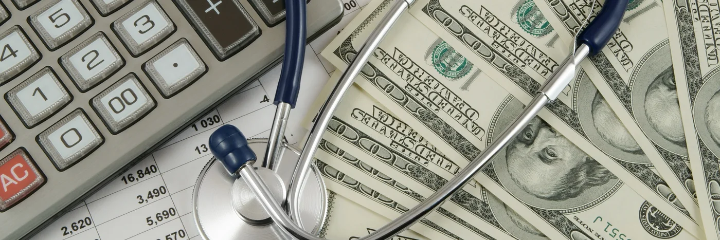 A calculator, a stethoscope and banknotes resting on a printed spreadsheet of figures.
